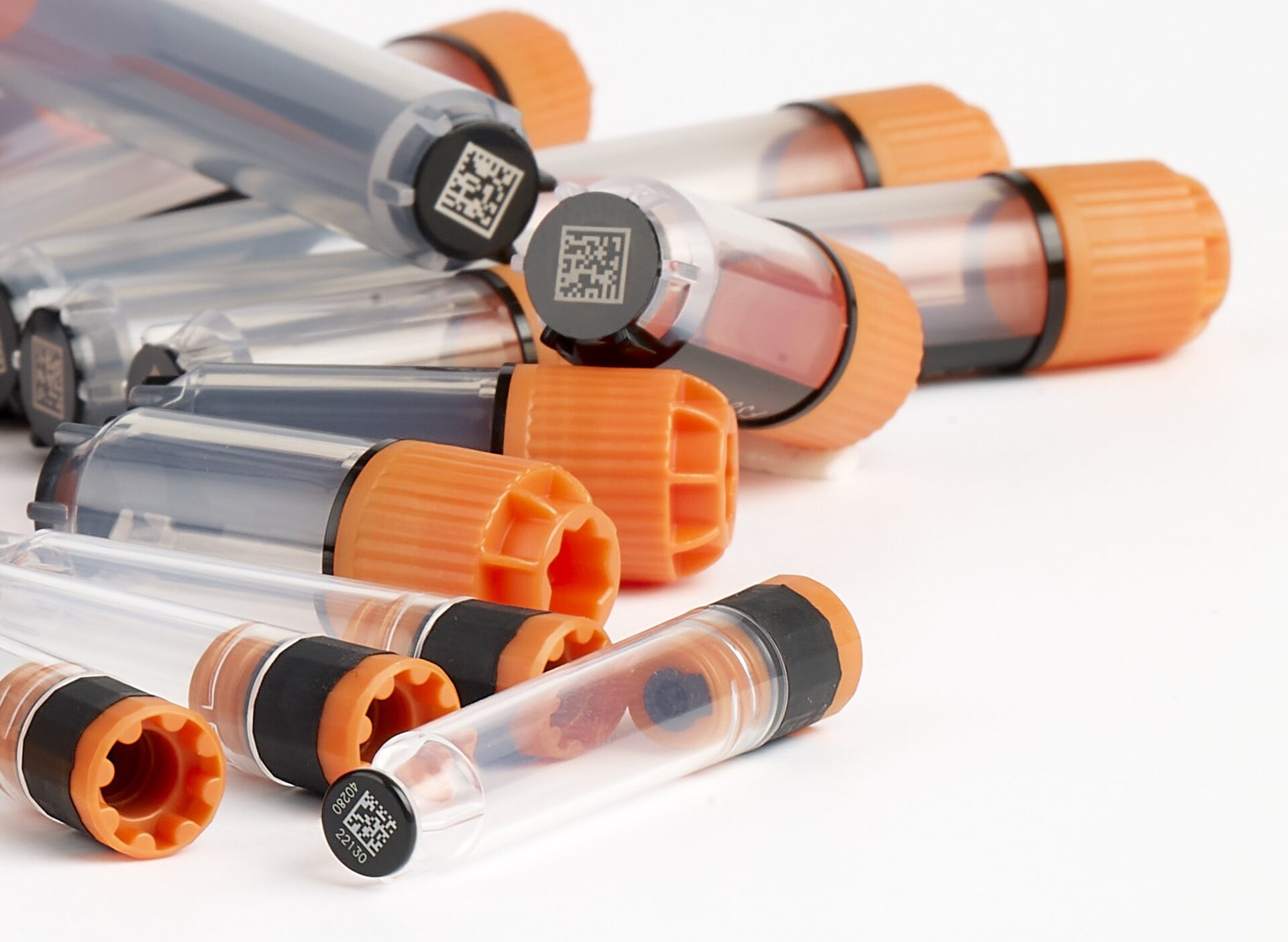 Small sample tubes with orange caps and barcodes, like the one you fill at home.